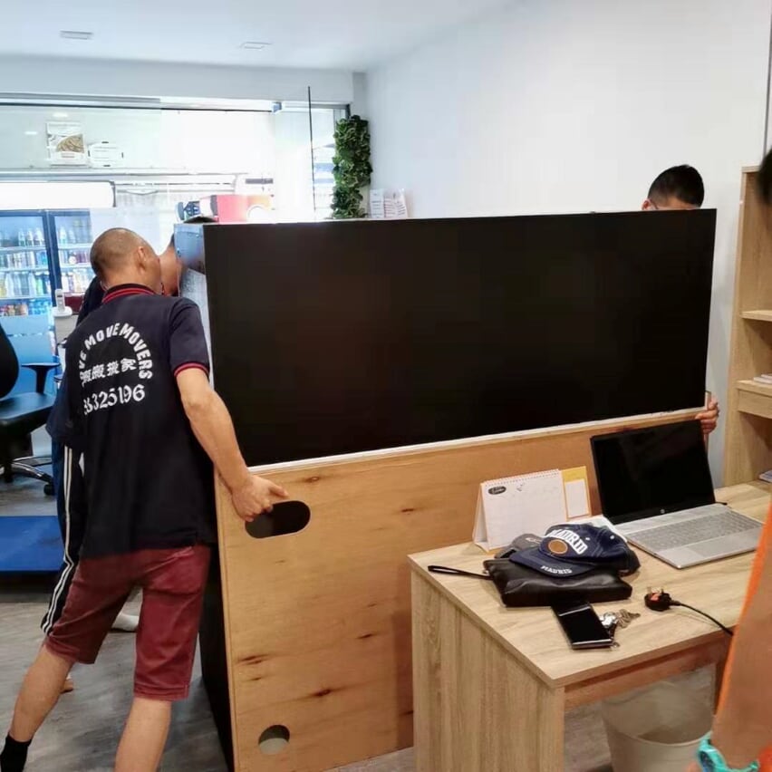 Move Move Movers crew carrying a large desk panel inside a Singapore office