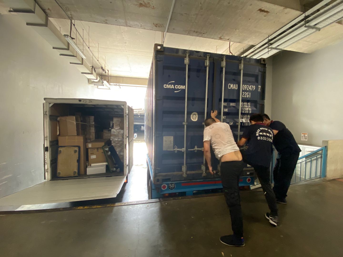 Crew positioning a shipping container beside a loaded box truck at a Singapore loading bay