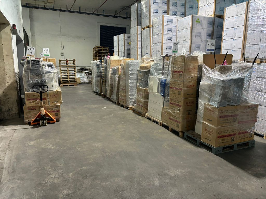 Wrapped office equipment and cartons staged on pallets in a warehouse